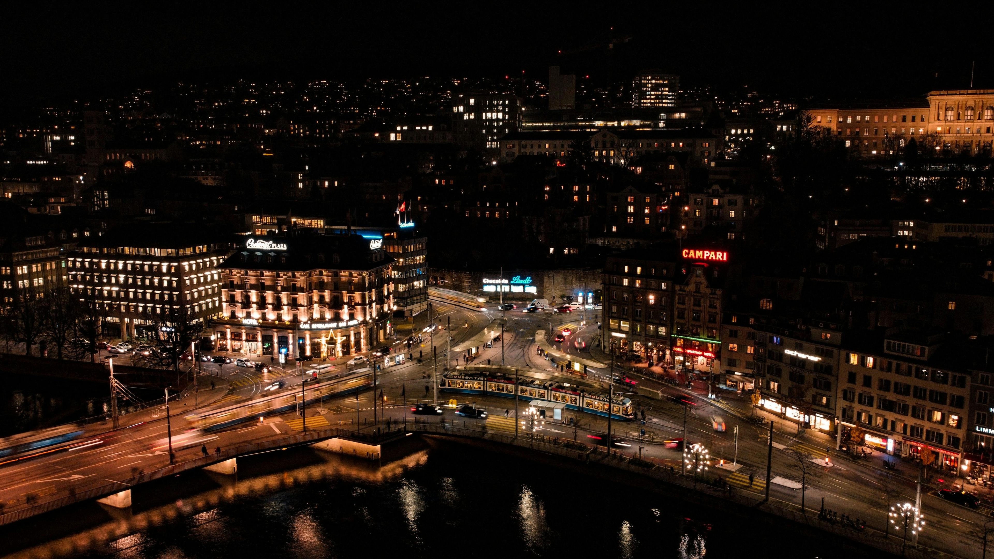 A night-time Zurich intersection of streets and a river seen from above